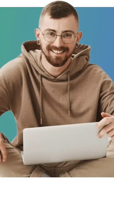 Image of a man with glasses and a beard sitting on the floor working on a laptop.