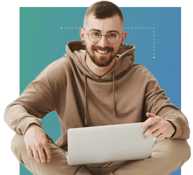Image of a man with glasses and a beard sitting on the floor working on a laptop.